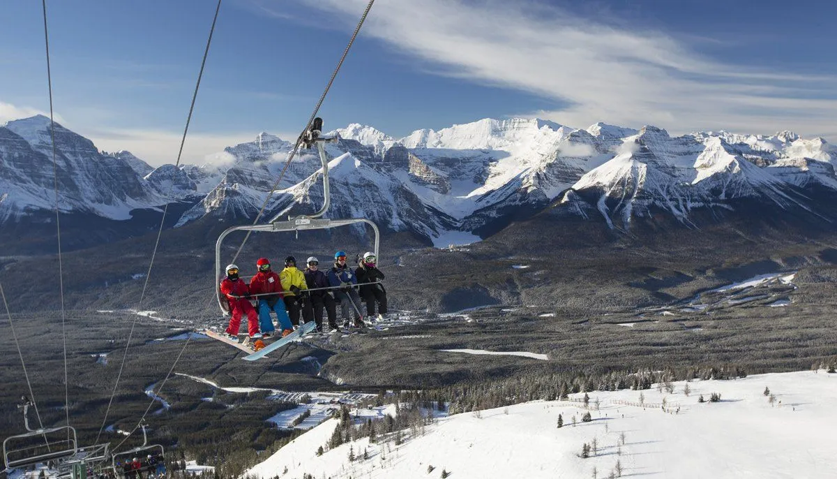 Ski lift chair carrying people over snowy mountains under a clear blue sky