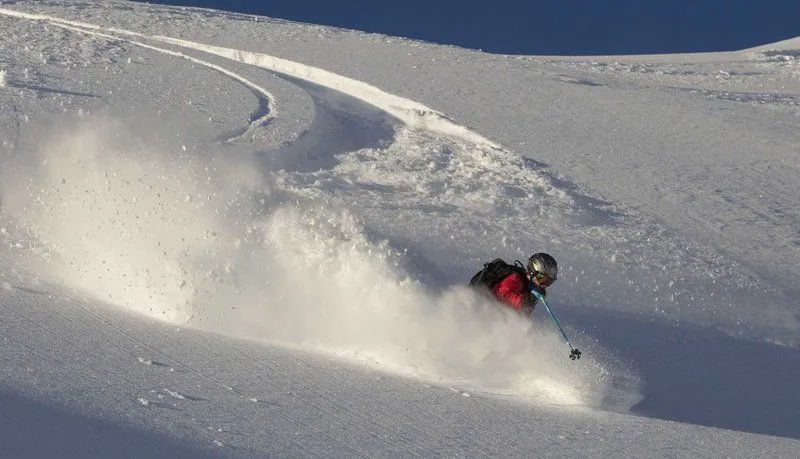 Skier in a red jacket carving through deep powder on a snowy mountain slope