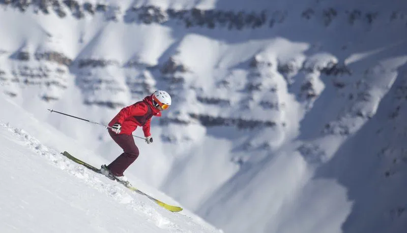 Skier in red jacket carving down a snowy mountain slope with ski poles trailing behind