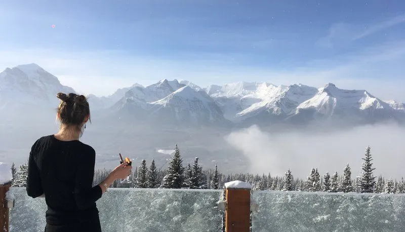 Person on a balcony facing snowy mountains and a misty alpine valley at sunrise