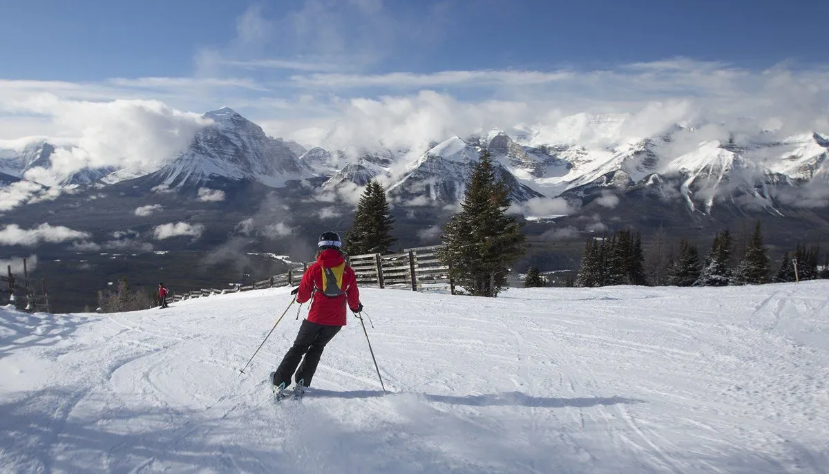Skier in red jacket gliding down a snowy slope with mountains in the background