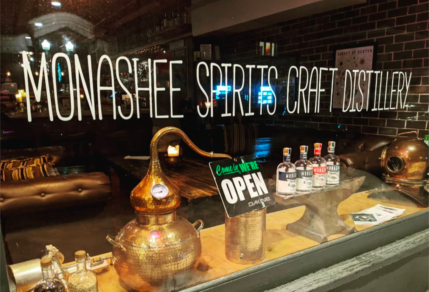 Monashee Spirits craft distillery storefront with copper still decor and “OPEN” sign in the window