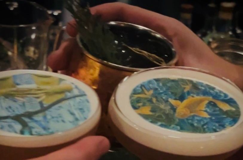 Hands holding three colorful round coasters or jars over a table in a dimly lit setting