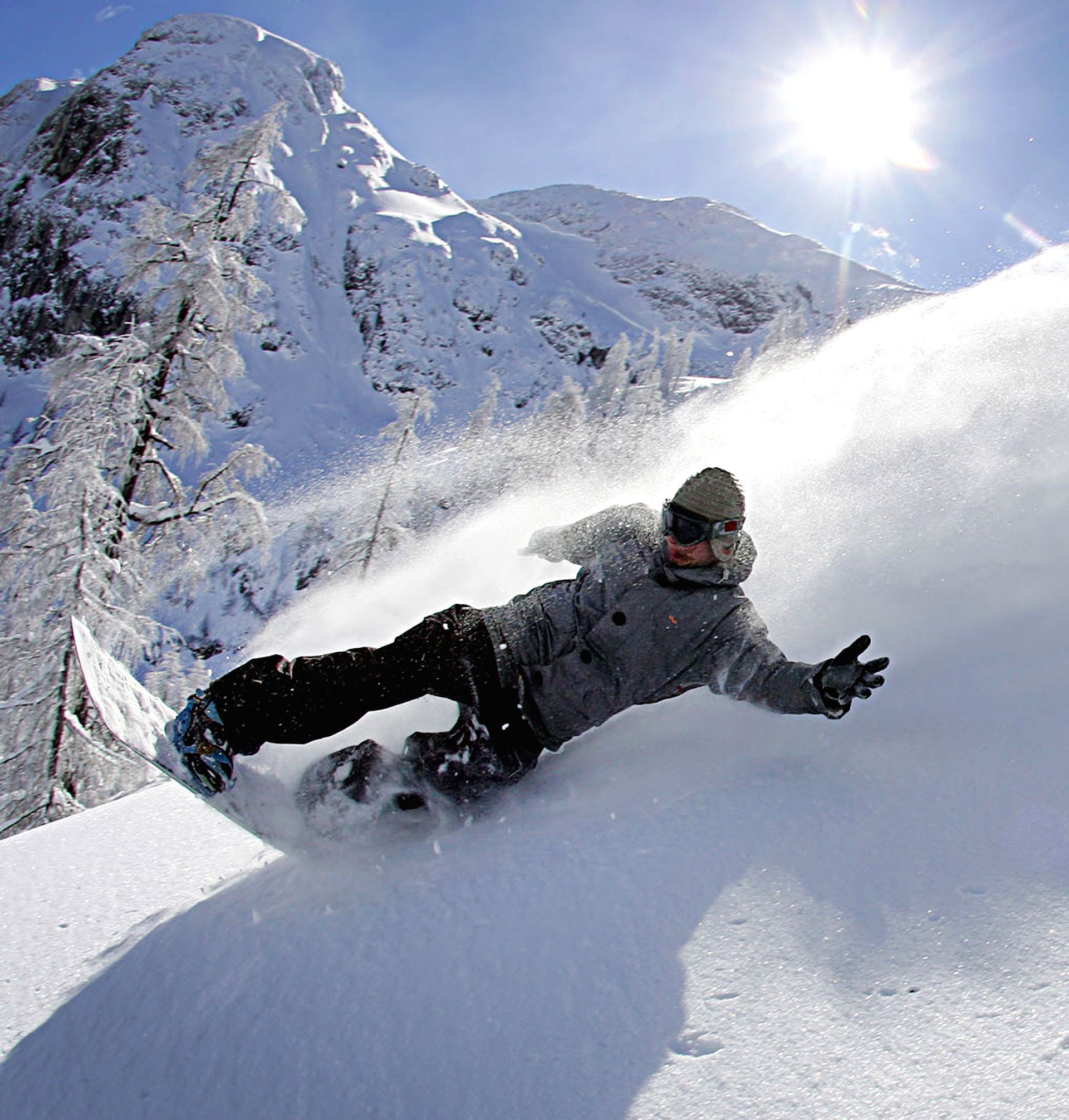 Snowboarder carving through deep powder on a sunny, snow-covered mountain slope