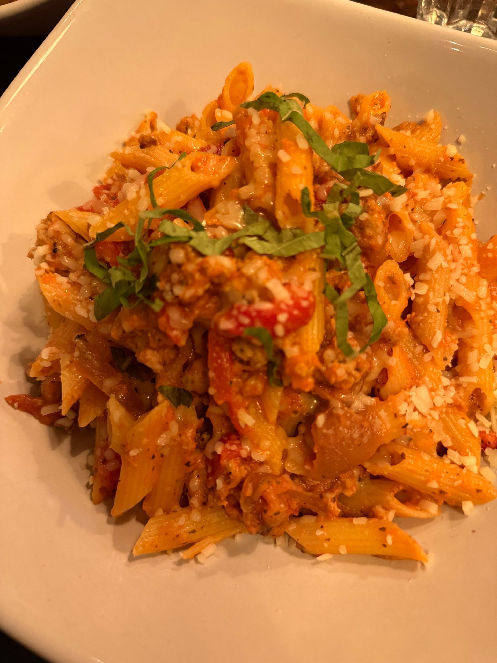 Penne pasta in red tomato sauce, garnished with chopped herbs, served in a white bowl.