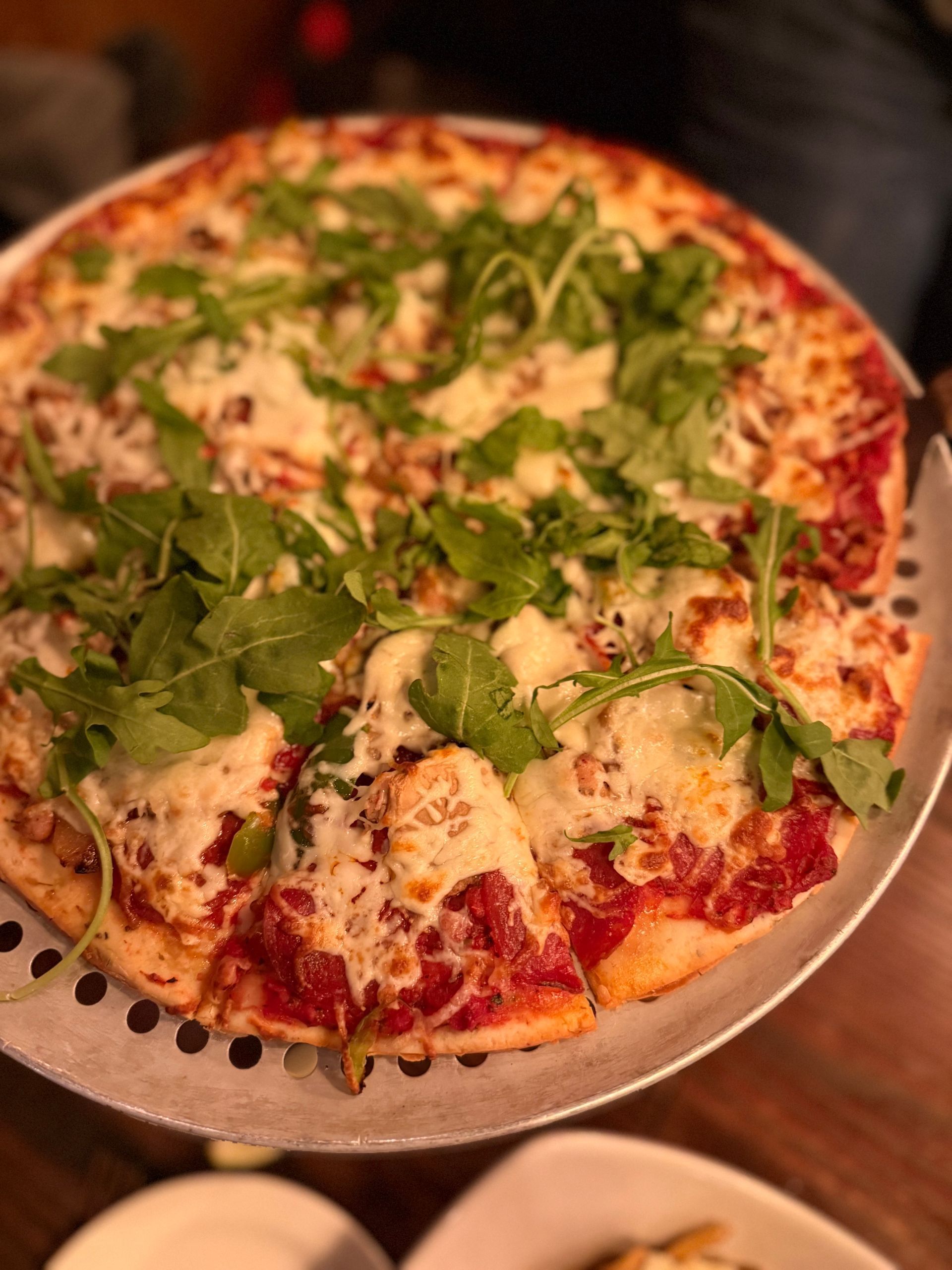 Pizza with melted cheese, red sauce, and fresh green herbs on a metal tray, with a small bowl beside it
