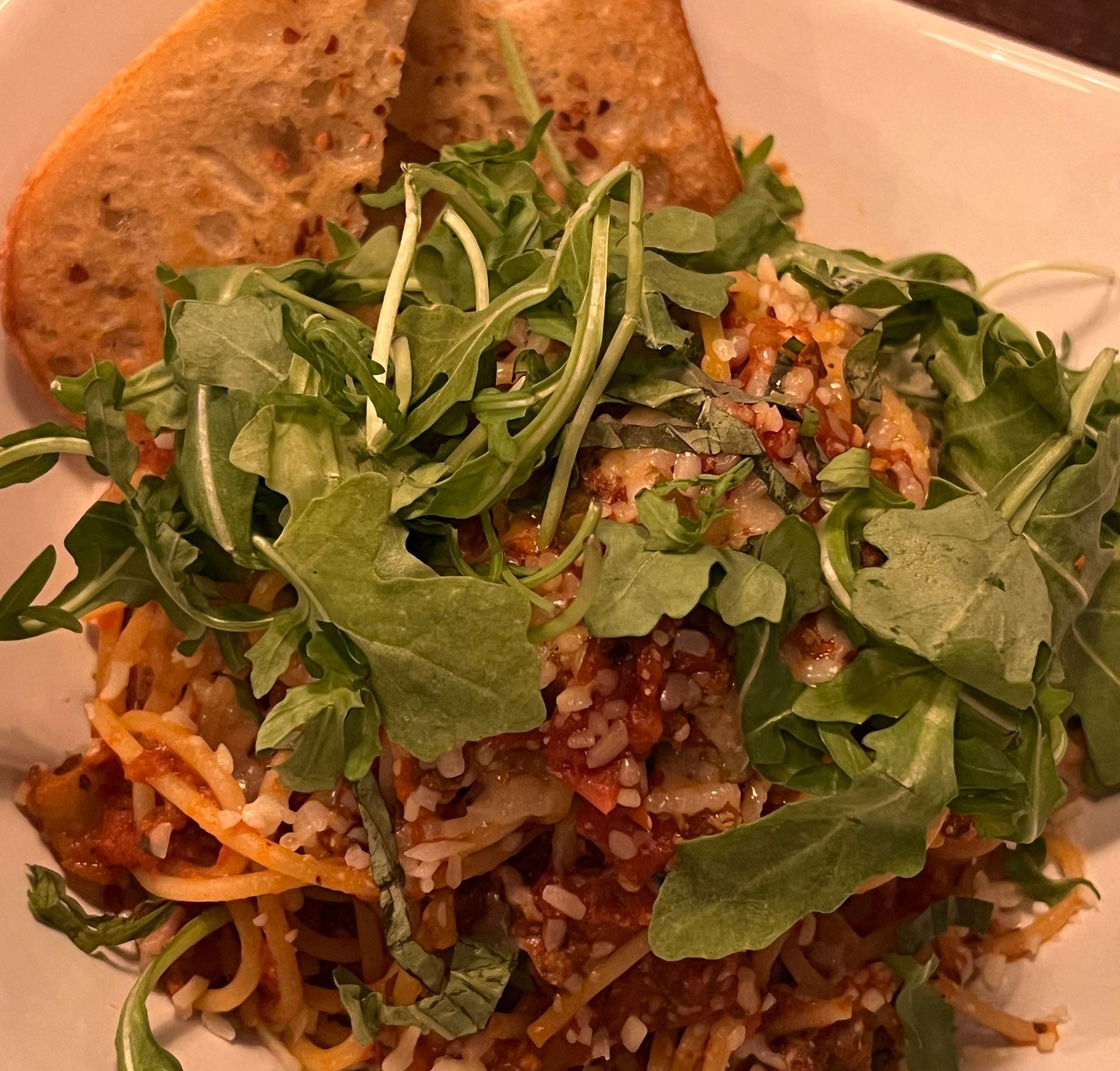 Pasta in tomato sauce topped with fresh arugula and grated cheese on a plate