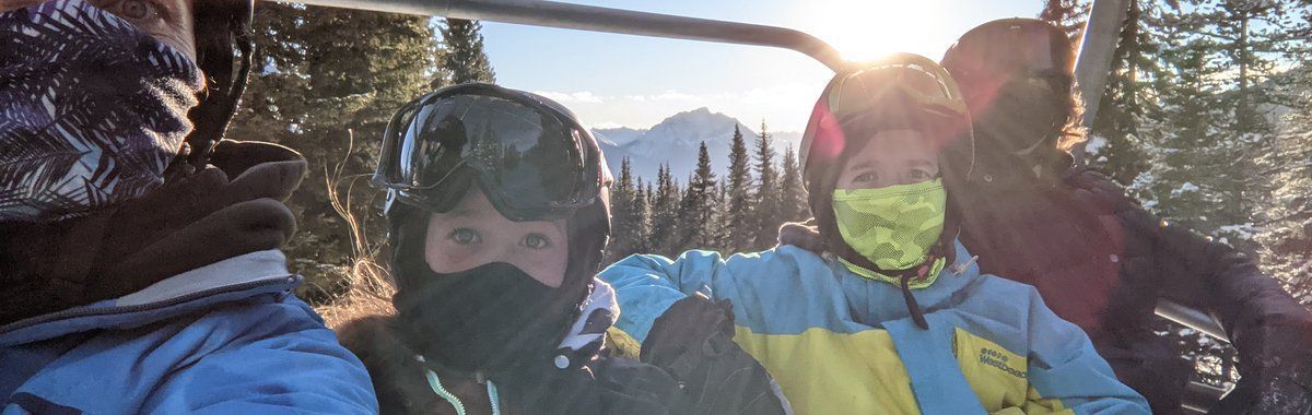 Three people in ski helmets and goggles posing in snowy mountains at sunset