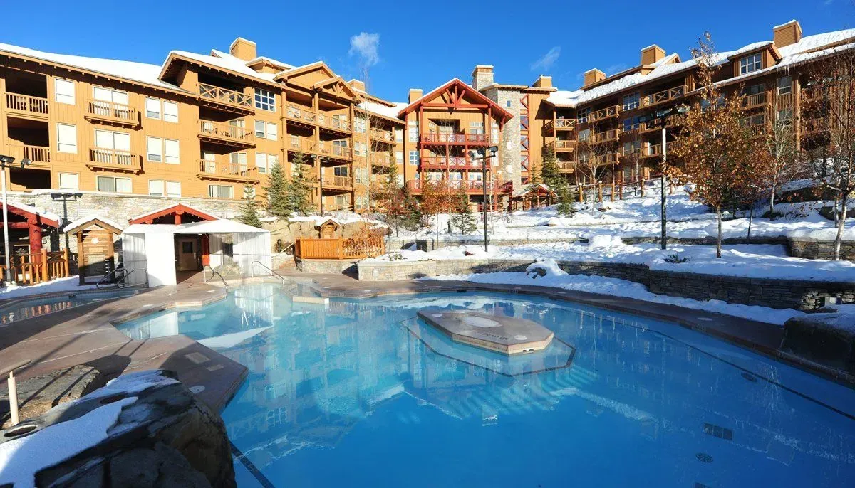 Snowy resort courtyard with a blue outdoor pool and surrounding lodge buildings