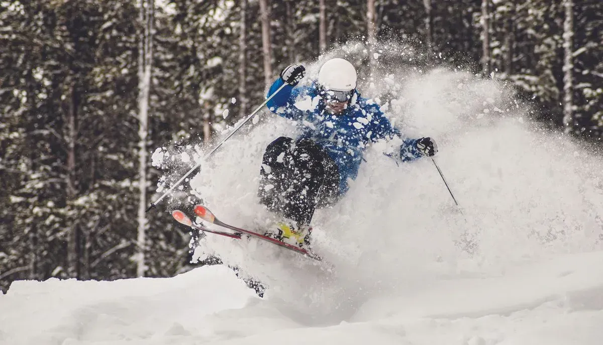 Skier in blue jacket carving through deep powder, sending up a burst of snow.