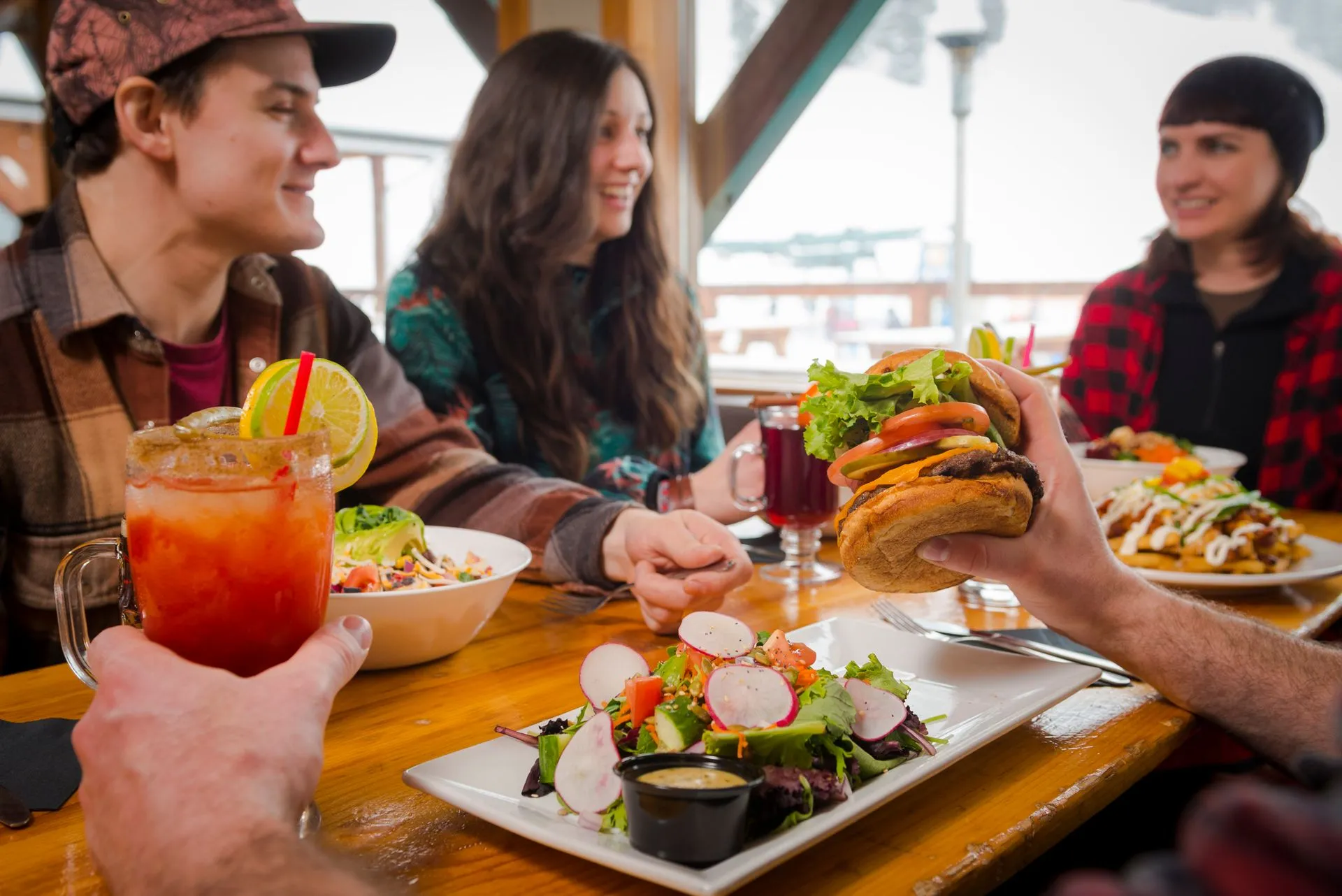 Friends sharing food and drinks at a restaurant table, smiling and toasting together