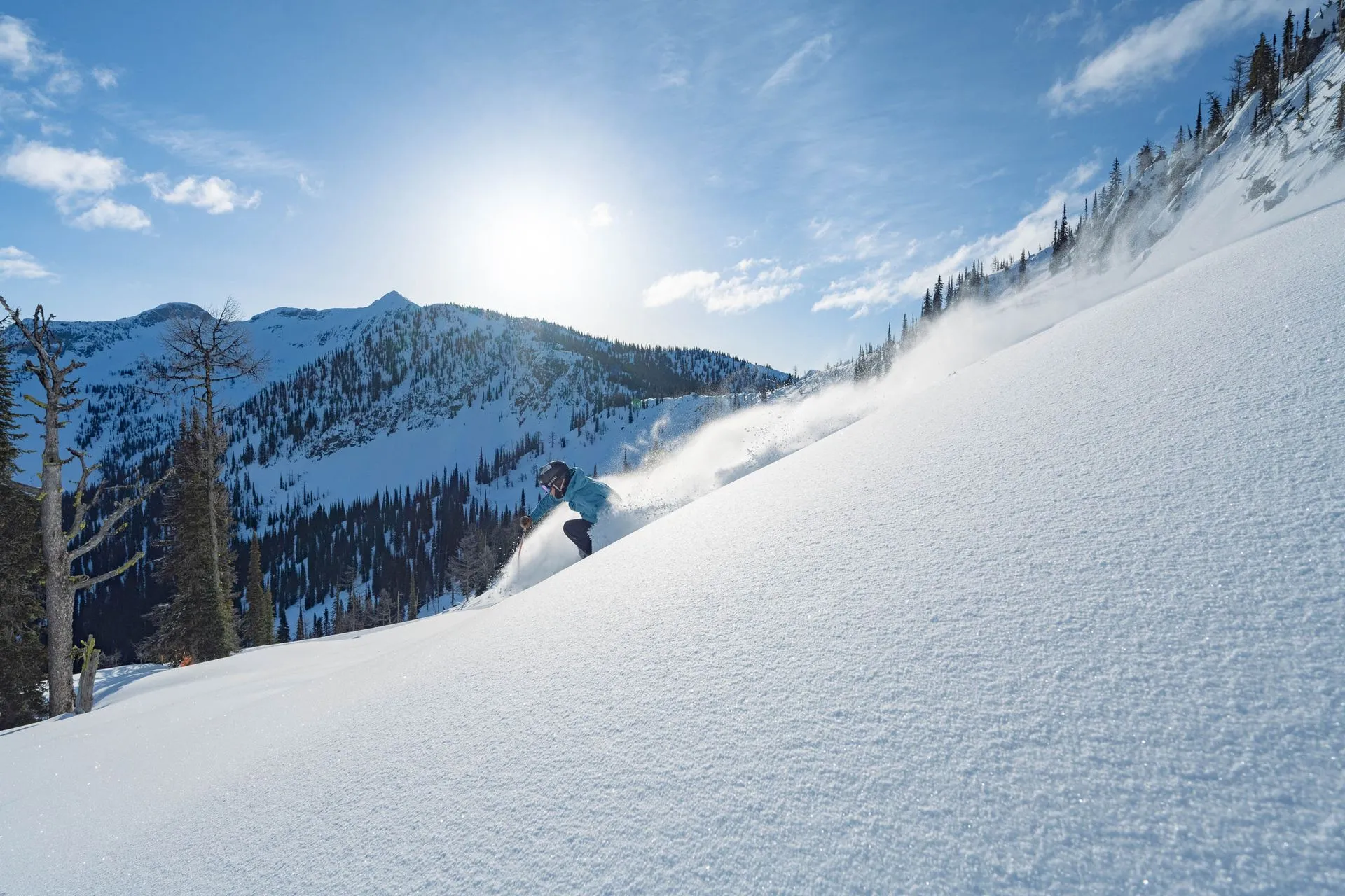 Snowboarder descending a bright, snowy mountain slope under a clear blue sky