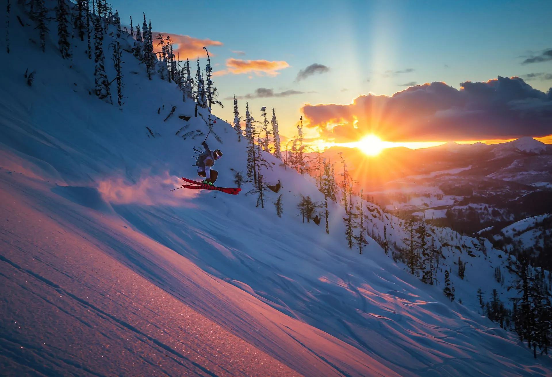 Sunset over snowy mountain slopes with silhouetted trees and glowing clouds