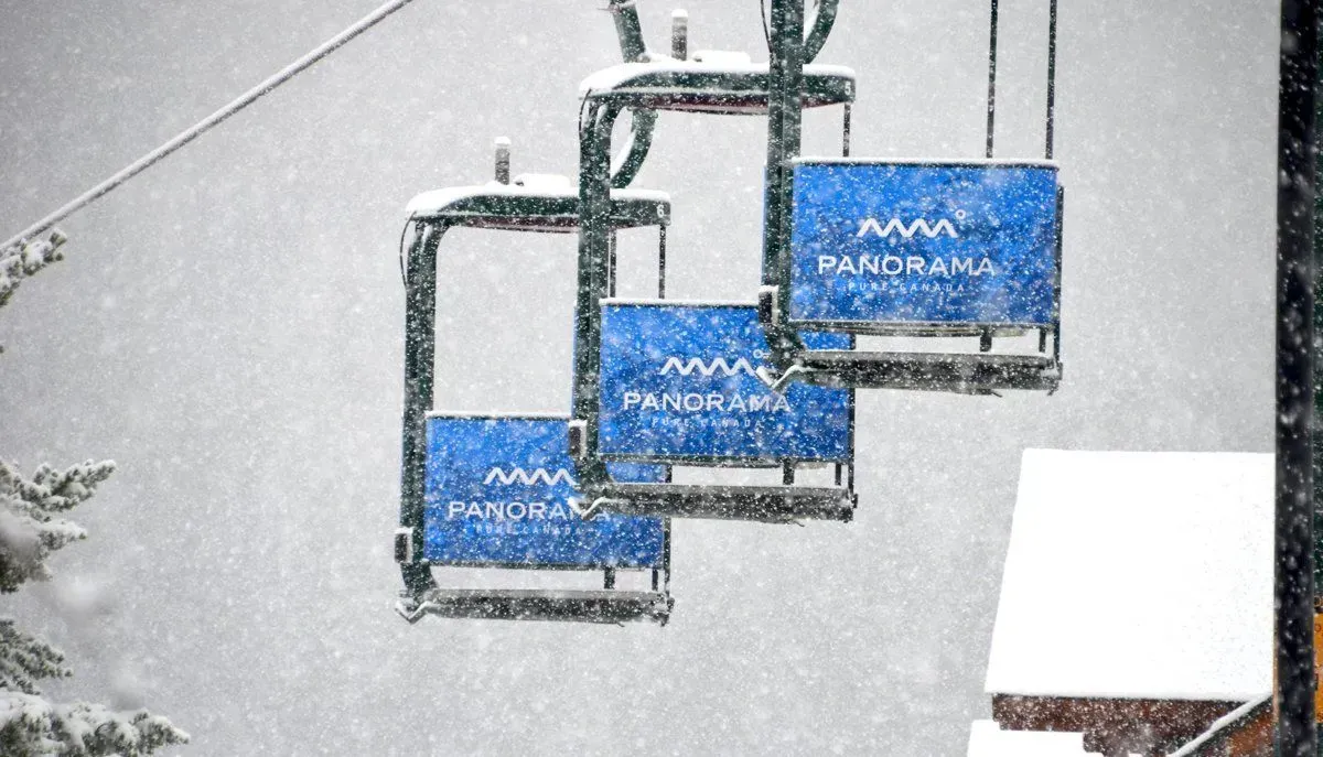Three blue ski lift chairs hanging from cables in falling snow