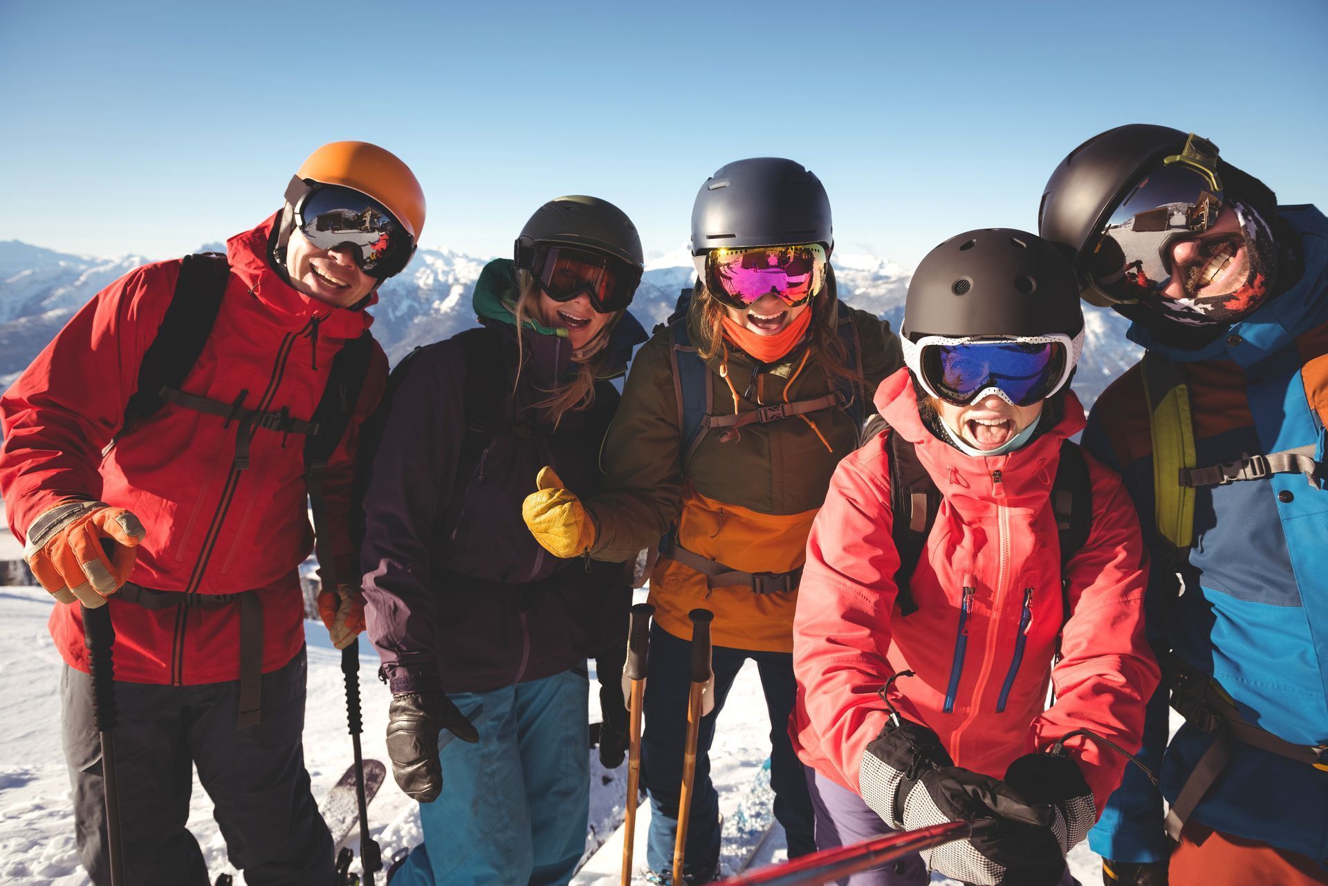 Five skiers posing on a snowy mountain, wearing colorful winter gear and ski goggles.