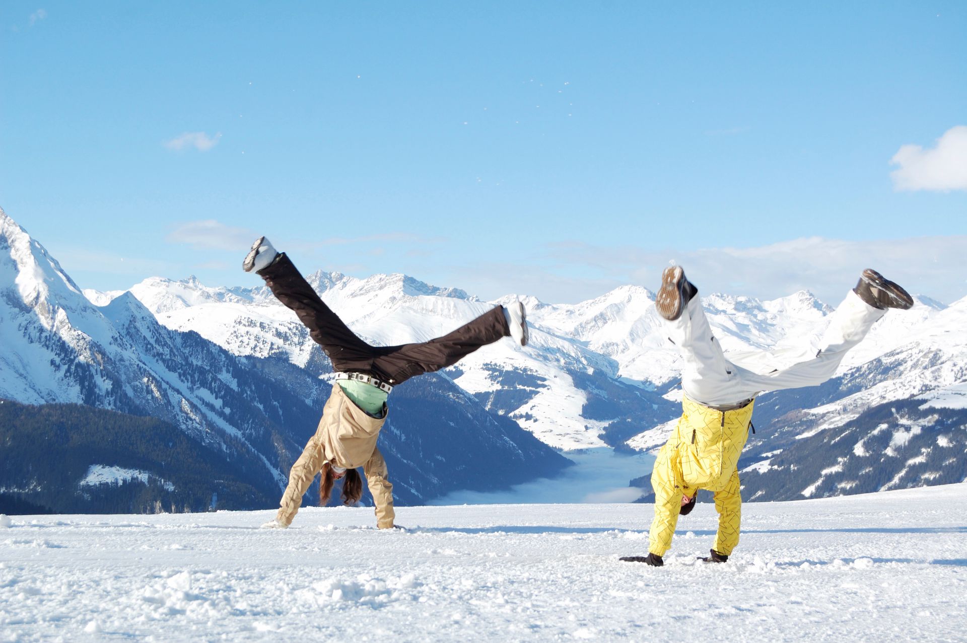Two people doing handstands on snow with mountains in the background