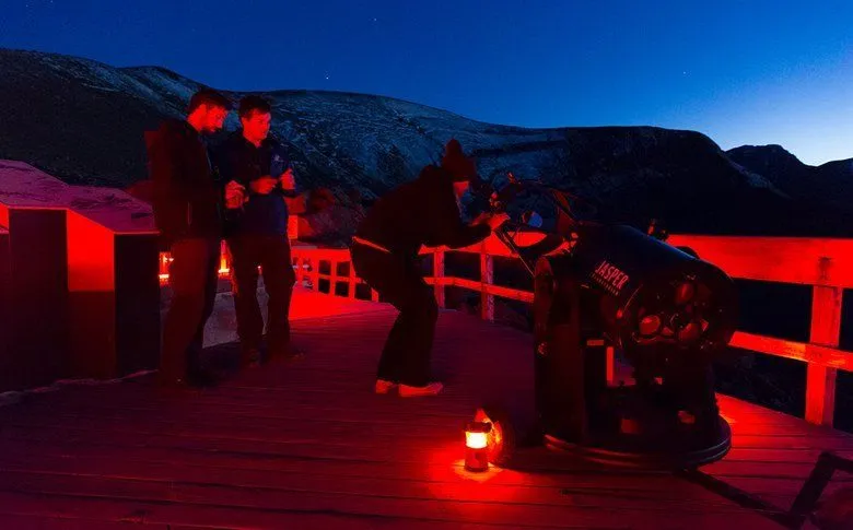 People on a lit deck at night, with red lights glowing against the dark sky.