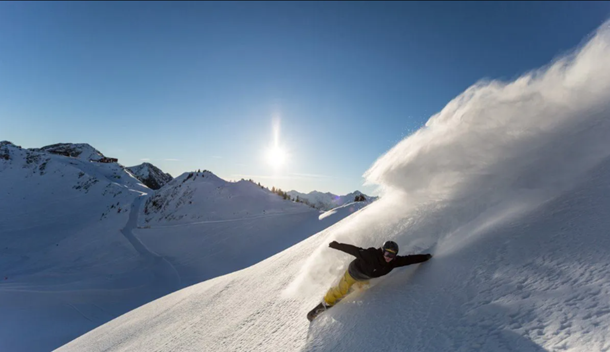 Snowboarder carving through fresh powder on a sunny mountain slope