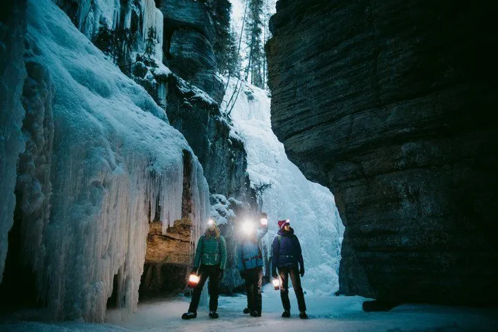 Three hikers with headlamps stand in a narrow icy canyon beneath towering rock walls.