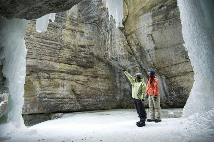 Two hikers in colorful jackets standing in a snowy rock canyon, one pointing upward