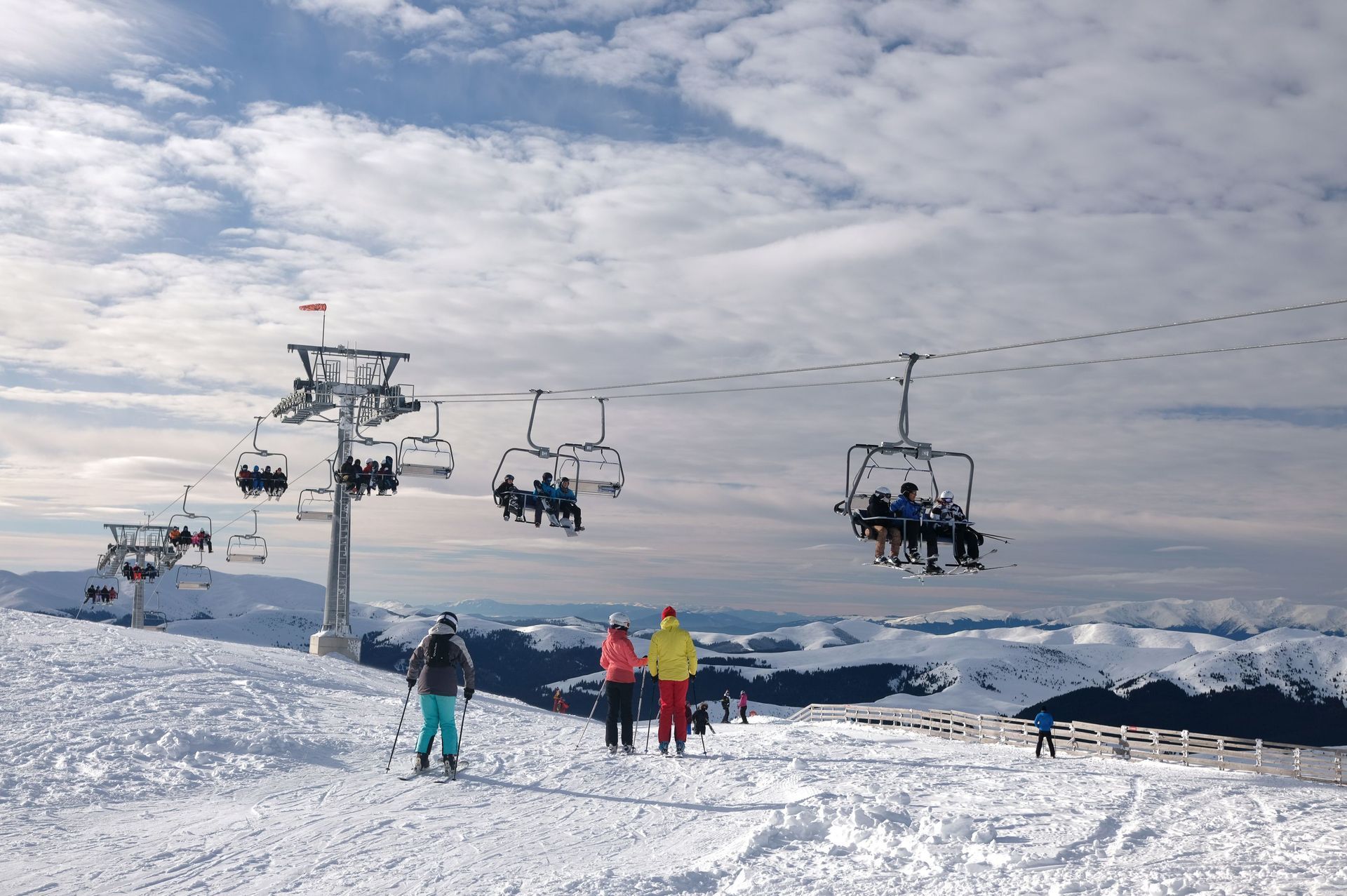 Skiers on a snowy mountain under chairlifts and a cloudy sky