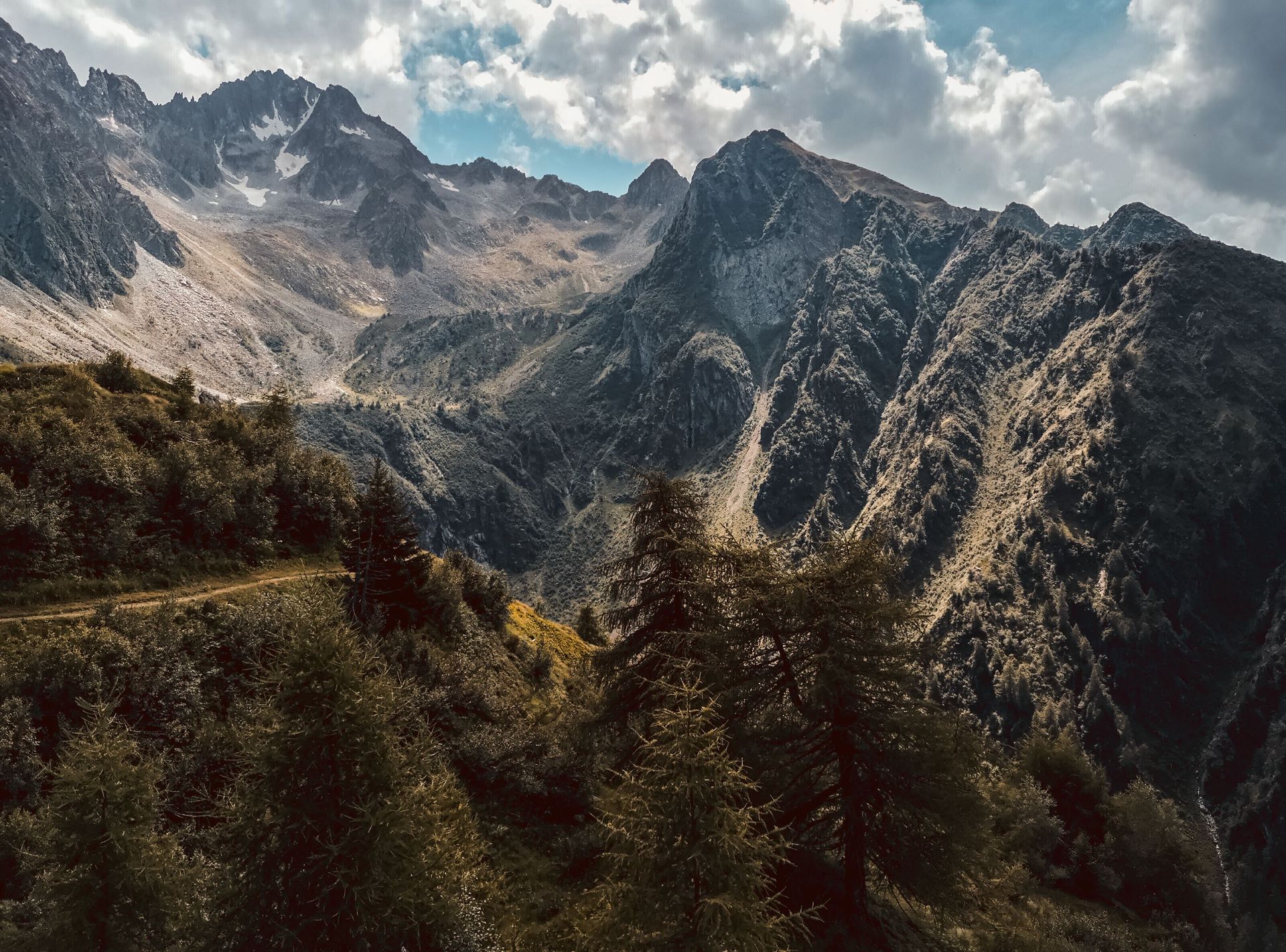Mountain range with rugged rocky peaks, dark forested slopes, and clouds overhead.