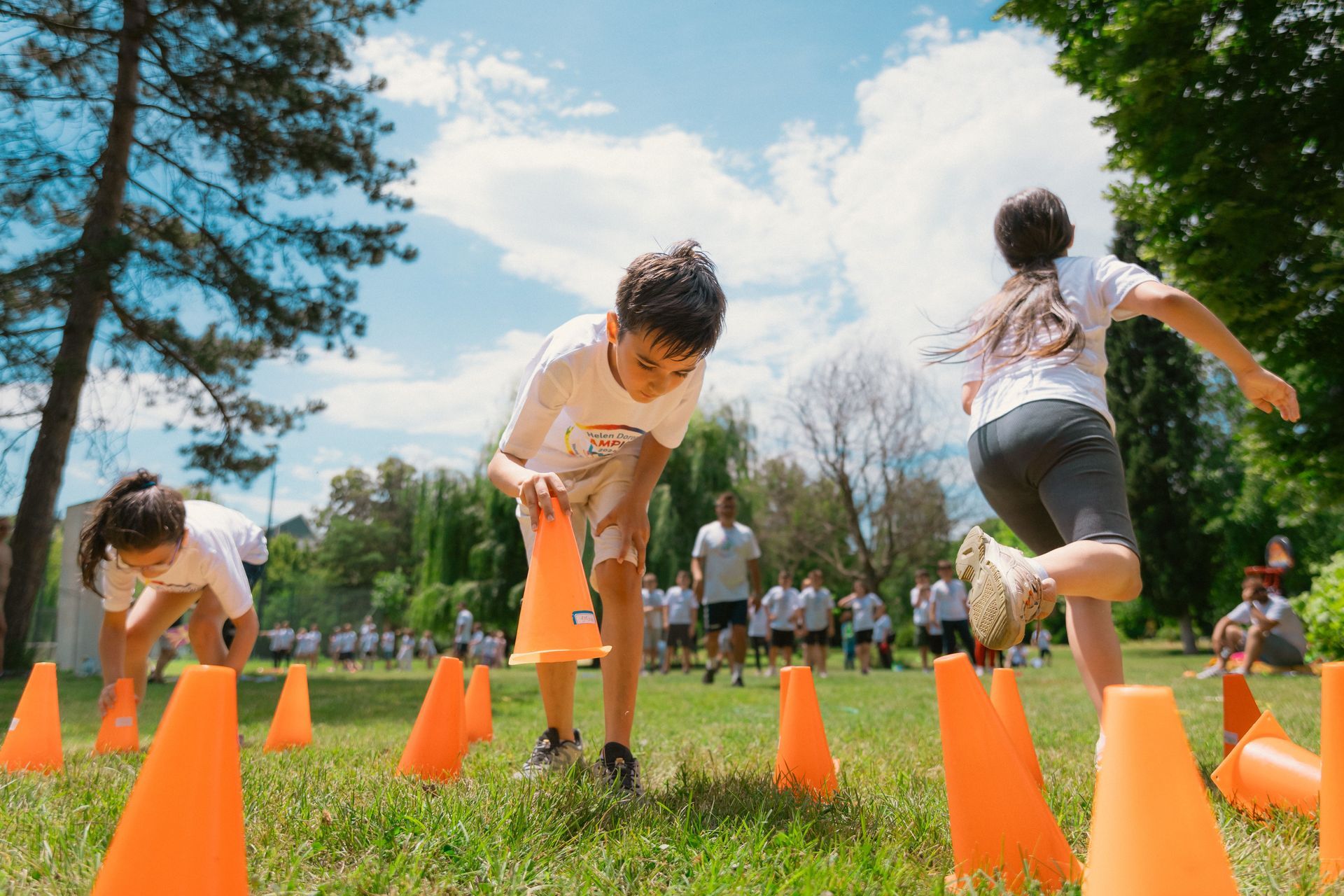 Children running through orange cones on a grassy field during an outdoor obstacle course
