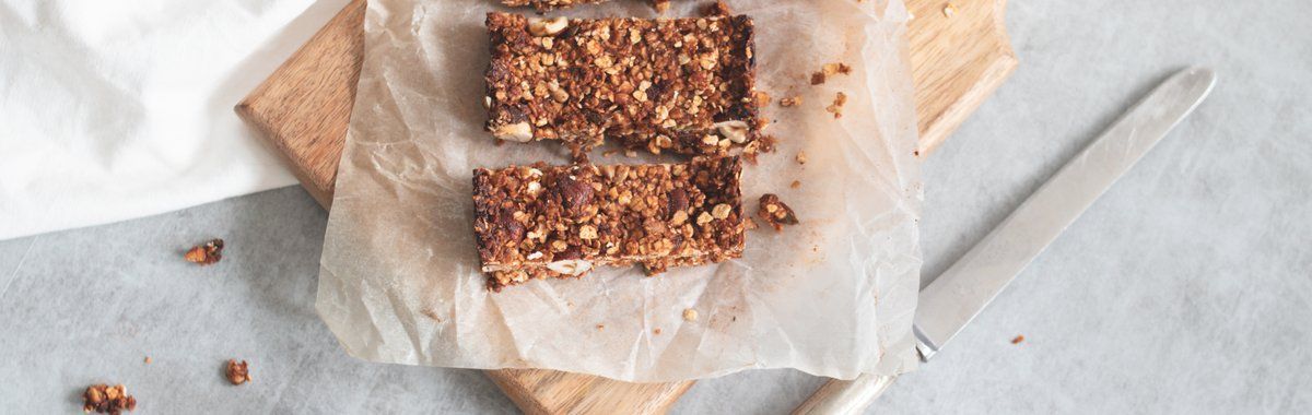 Chocolate granola bars on parchment paper, with a knife on a light countertop.