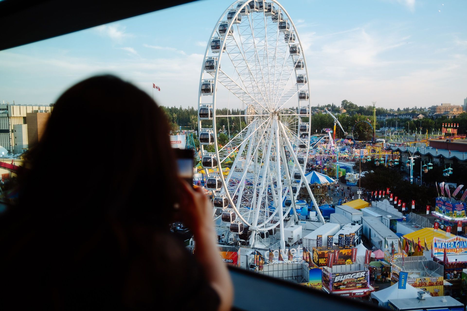 Silhouette of a person viewing a lit Ferris wheel at an outdoor fair at dusk