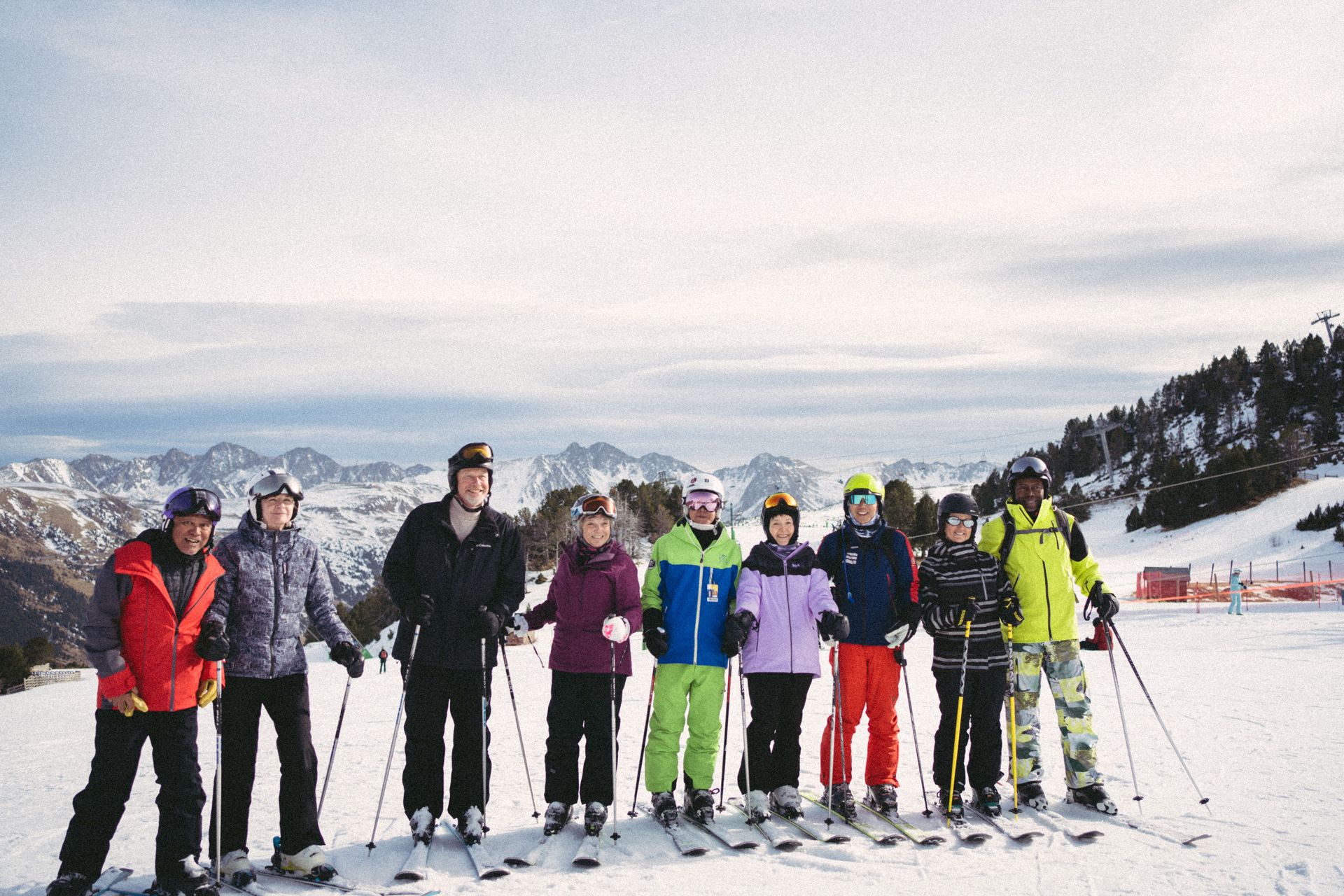 Ski group posing on a snowy mountain with skis and poles, snow-covered peaks in the background