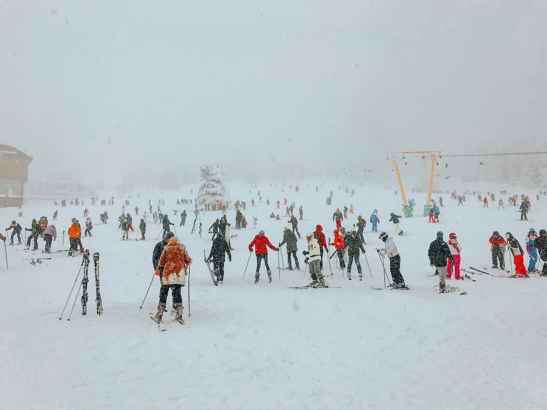 People skiing and standing in a snowy ski area with fog and lift towers in the background