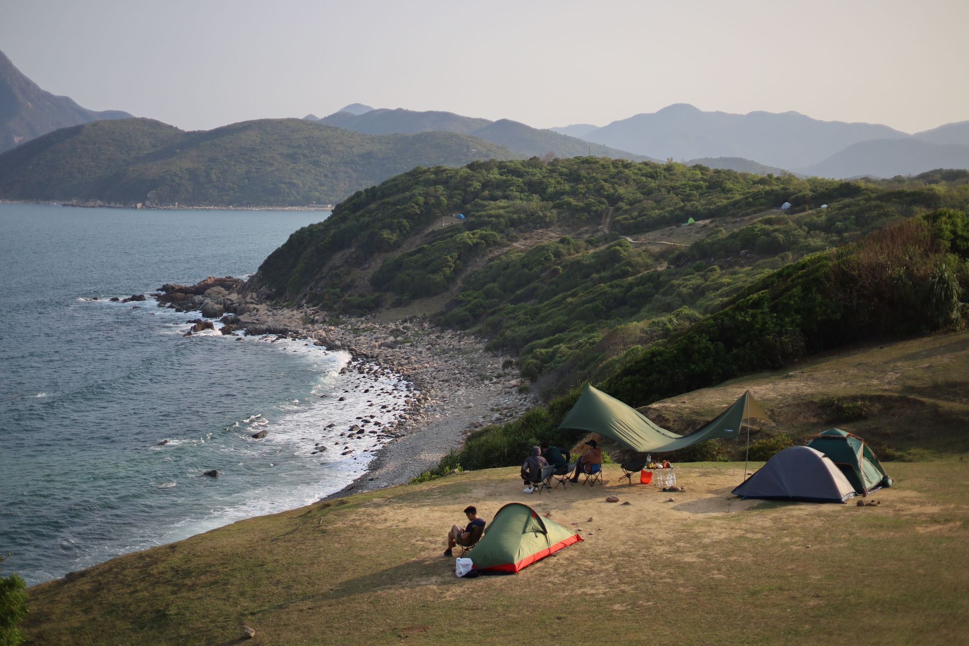 Campsites on a grassy cliff overlooking a rocky shoreline and calm blue sea at sunset