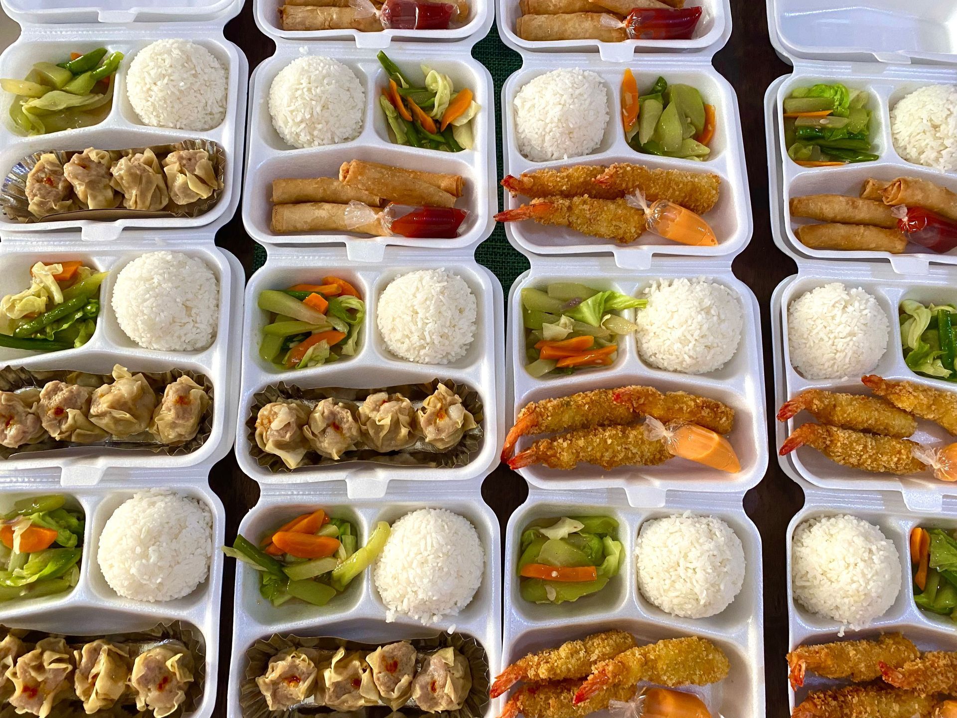 Rows of packaged meal trays with rice, vegetables, and meat in clear plastic containers