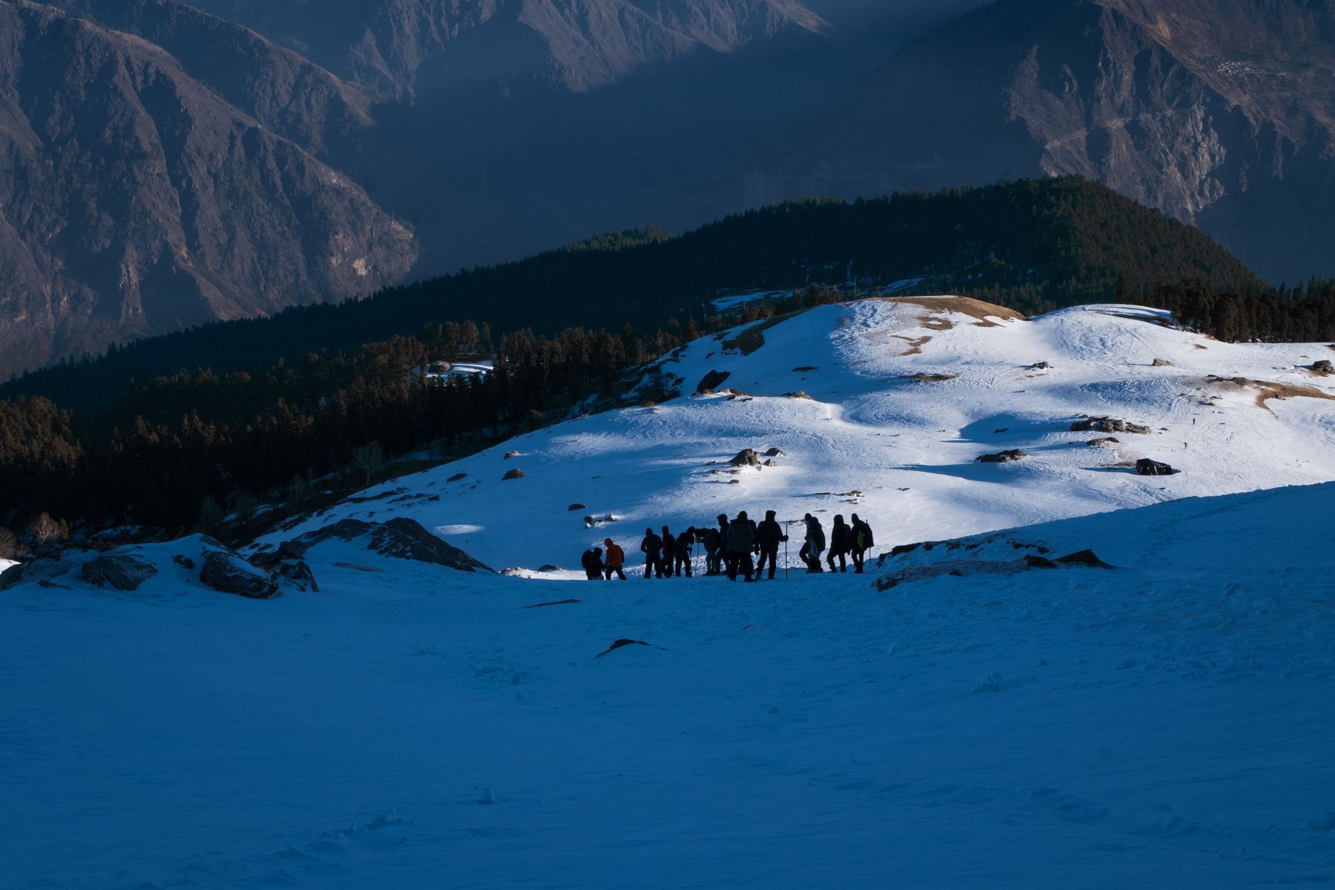 Snow-covered mountain meadow with a small group of hikers under a blue sky