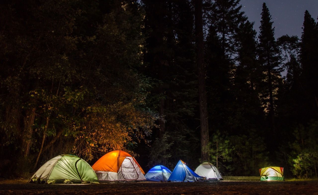 Small campsite at dusk with lit colorful tents in a dark forest clearing