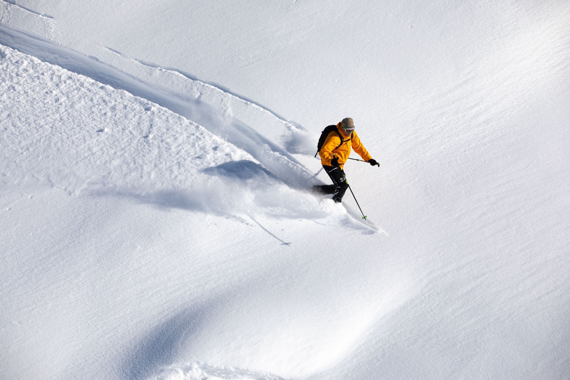 Skier in orange jacket carving turns through fresh powder on a snowy slope