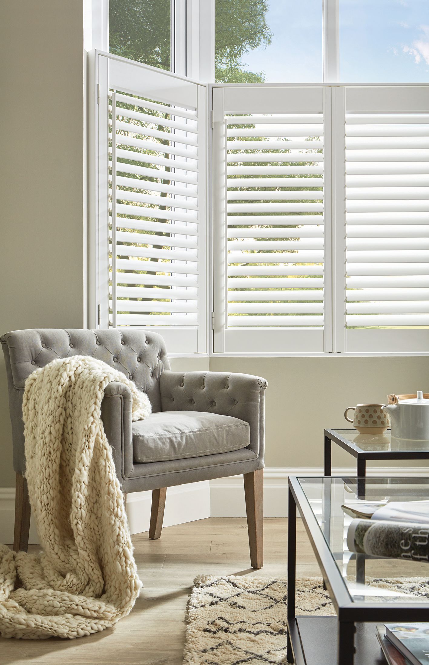 A cozy living room with a tufted chair, throw blanket, and white shutters.
