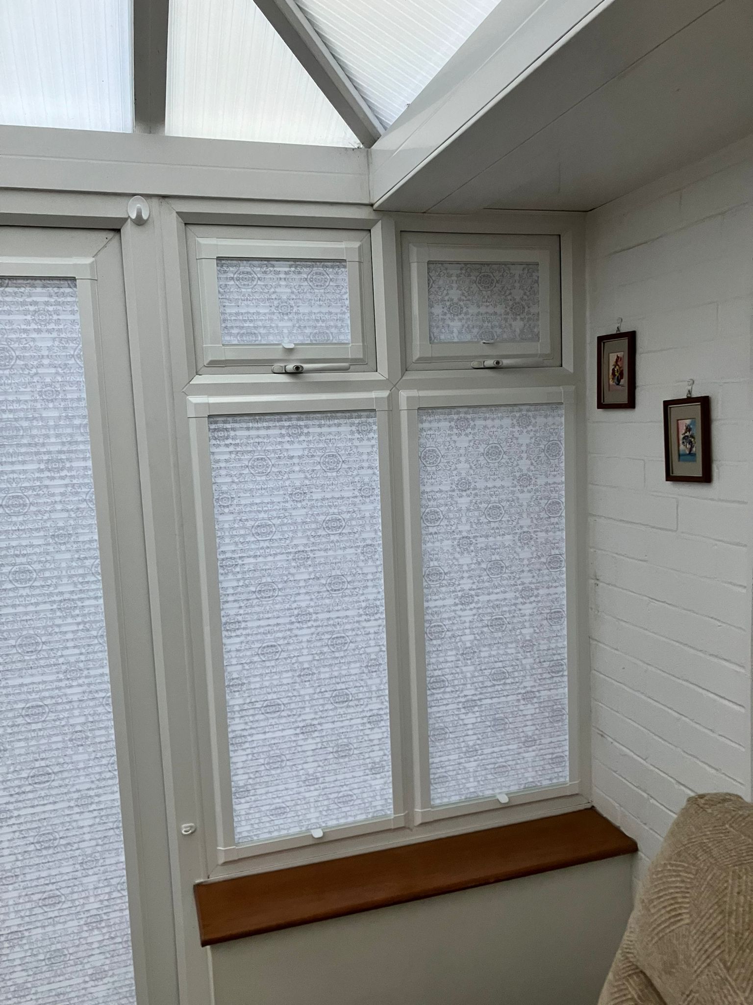 White-framed windows with blinds in a sunroom. Wooden sill, white brick wall, and small framed art.