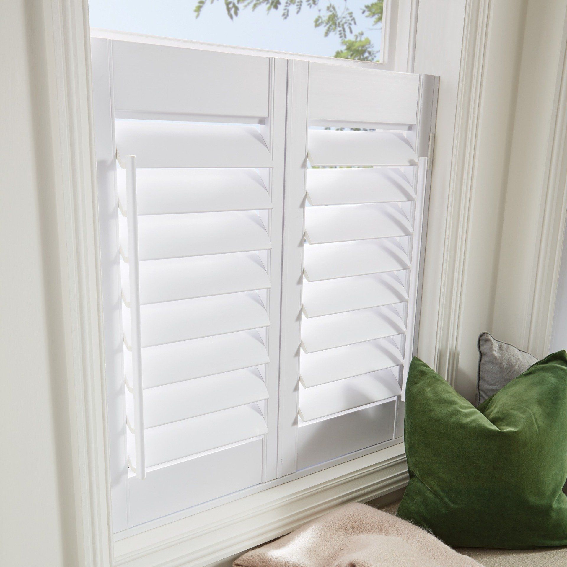 White shutters in a window, partially open. Green pillow on the window seat.