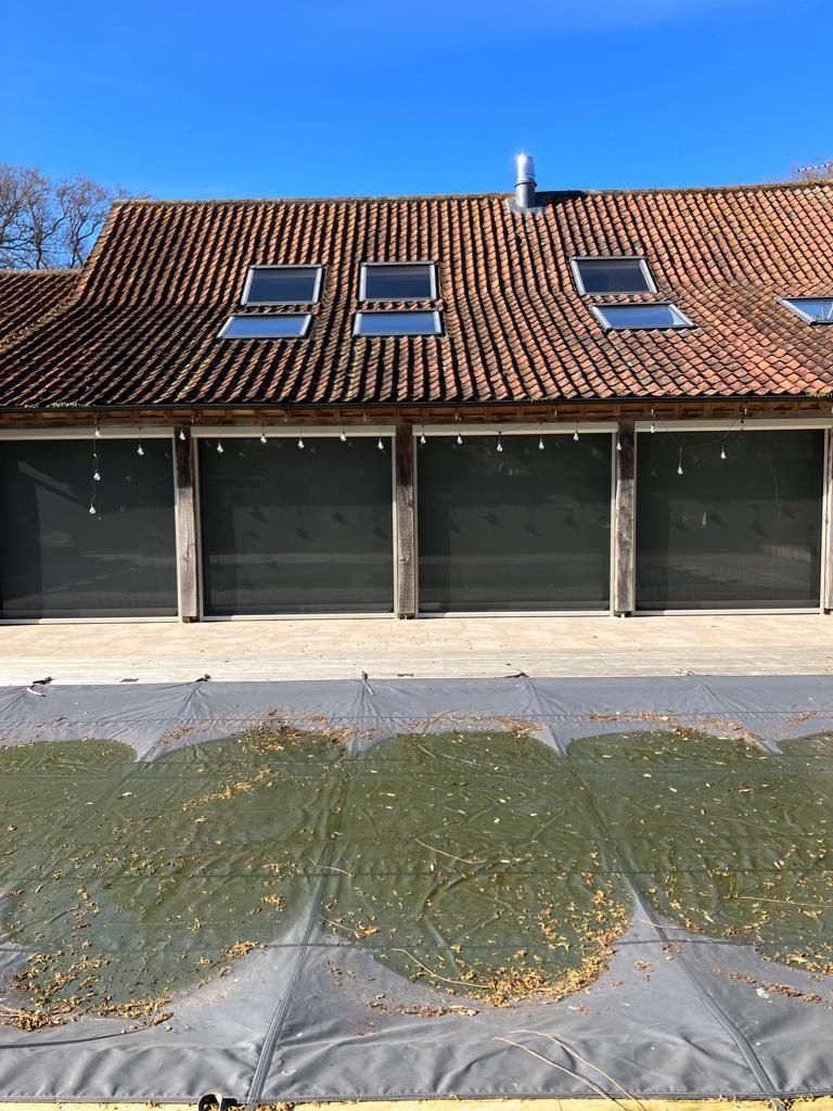 Barn with red-tiled roof, four skylights, and closed garage doors; pool covered with debris in front.