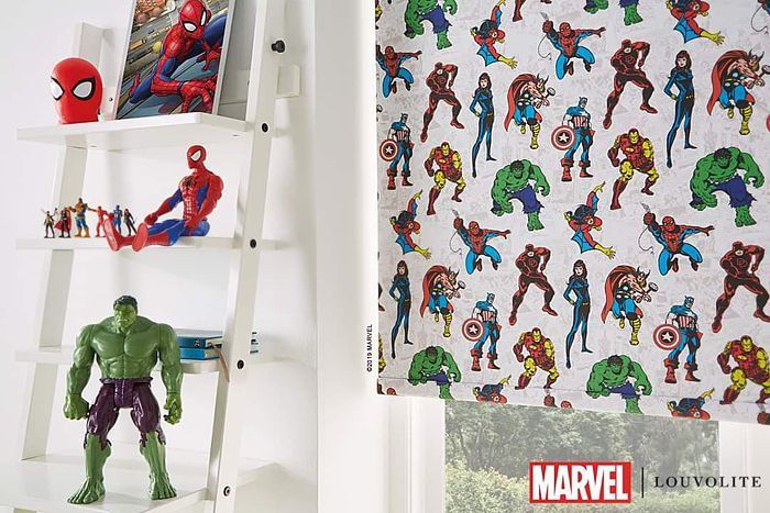 Superhero-themed room with ladder shelf displaying toys and artwork. Roller blind with repeating Marvel character print.