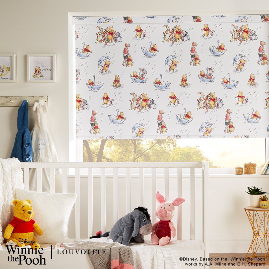Nursery with Winnie the Pooh roller shade, crib, stuffed toys, and artwork. White, beige, and blue colors.