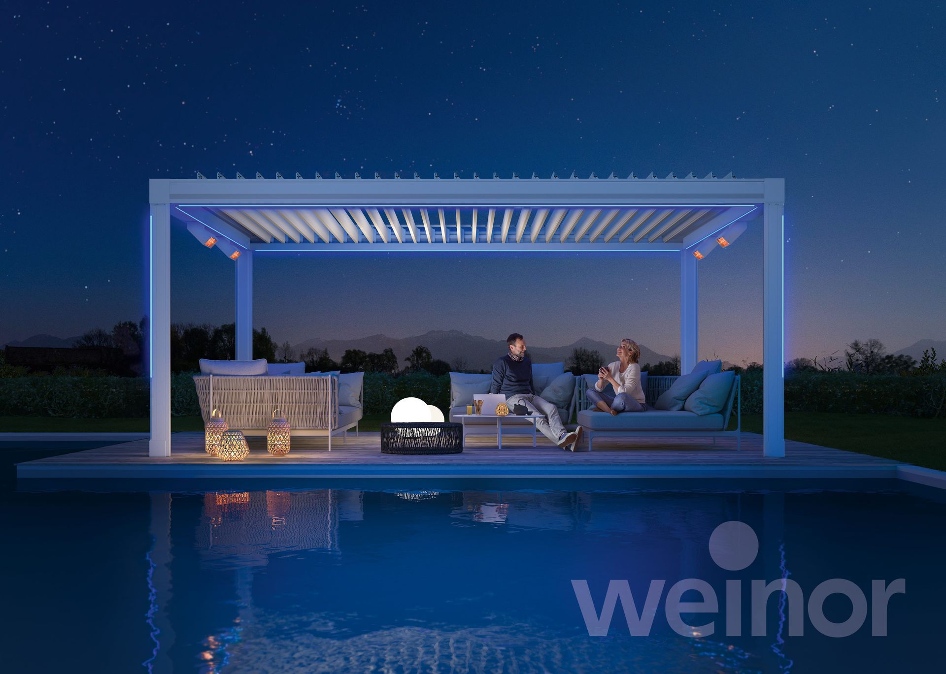 Pergola with blue lighting over pool, two people seated on a sofa. Fire pit and bar area are visible.