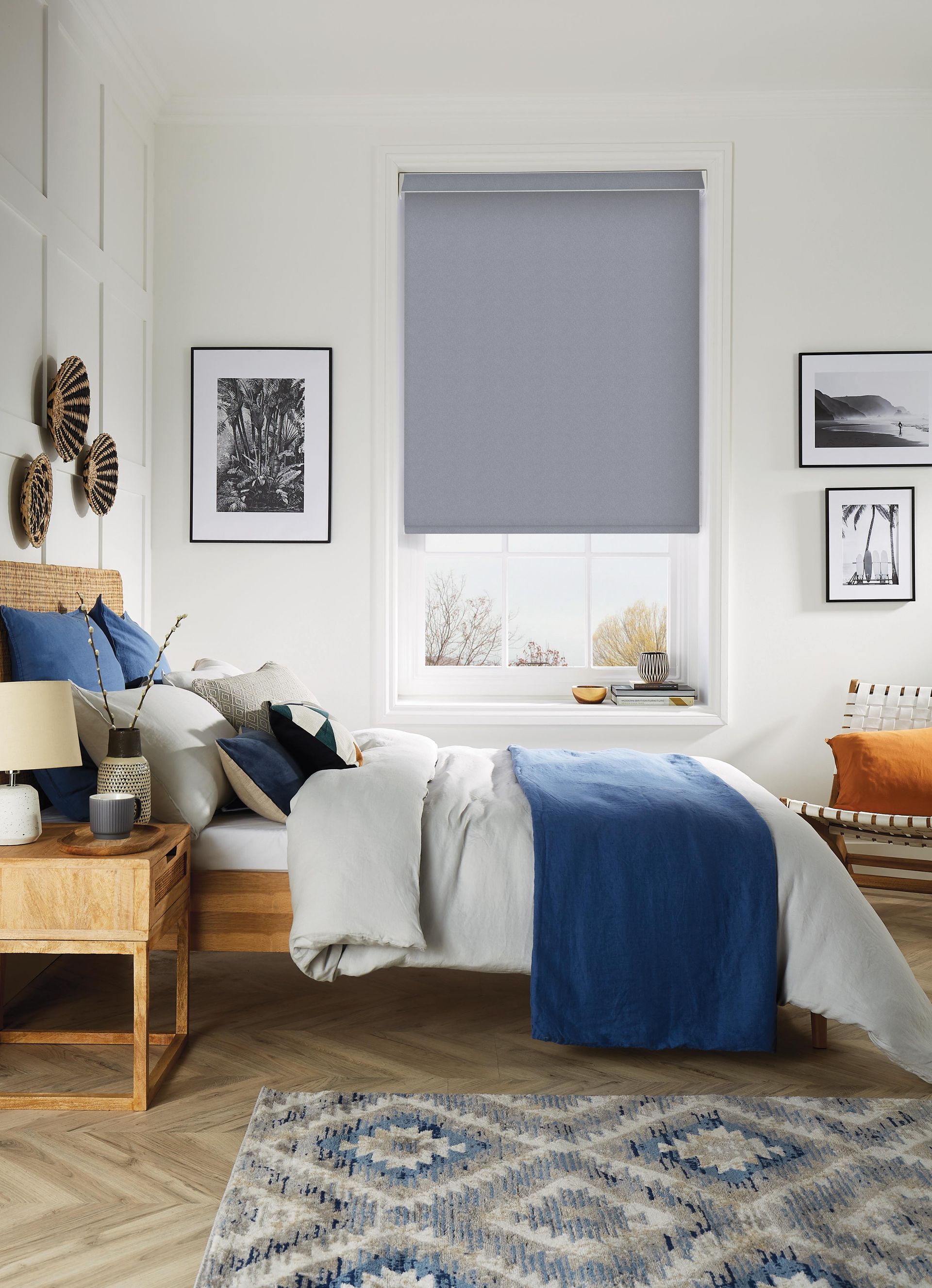 Bedroom with bed, blue blanket, rug, and window with gray blind.
