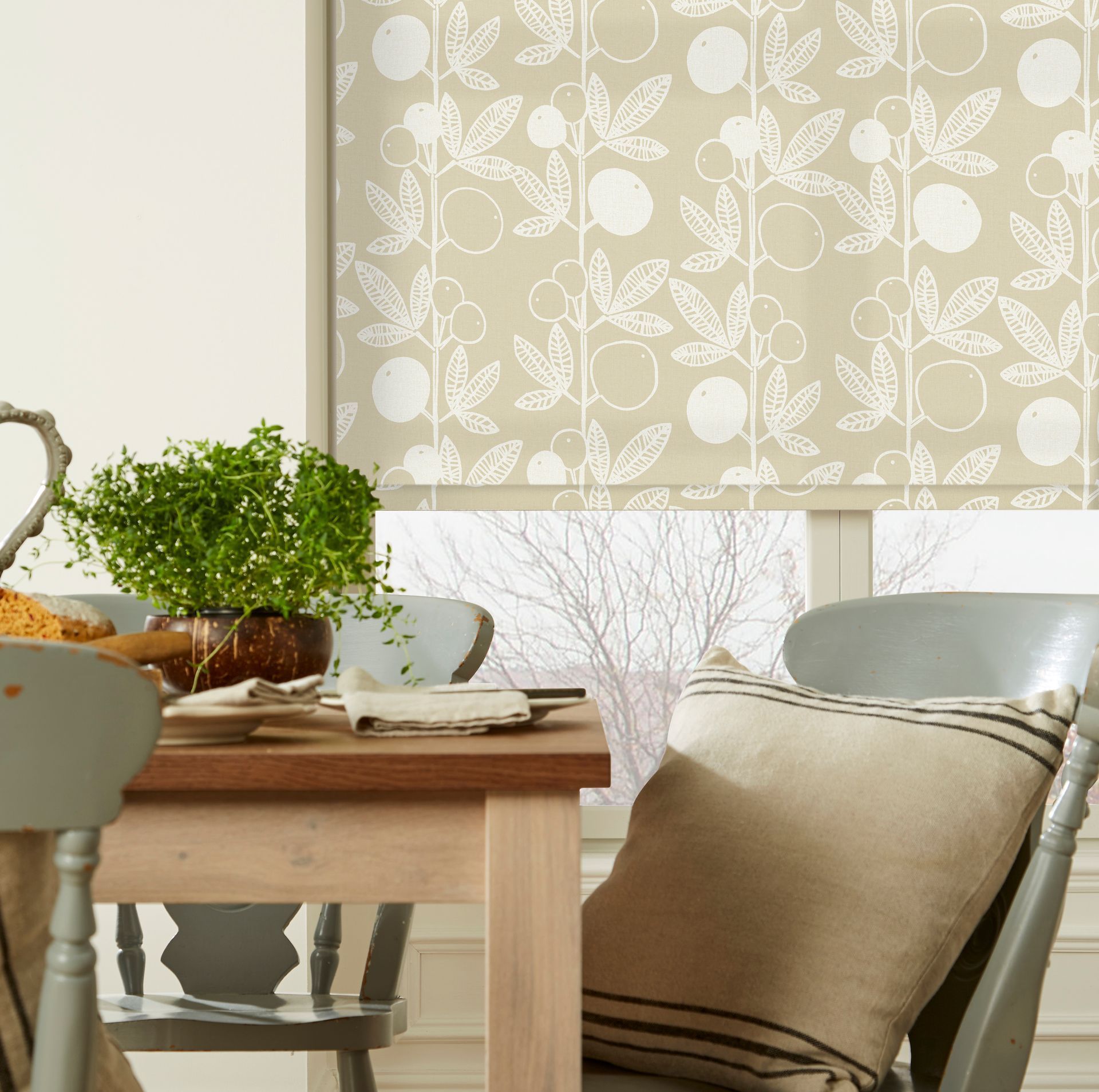 Dining room scene: table set with plant, patterned blinds, gray chairs, window view.