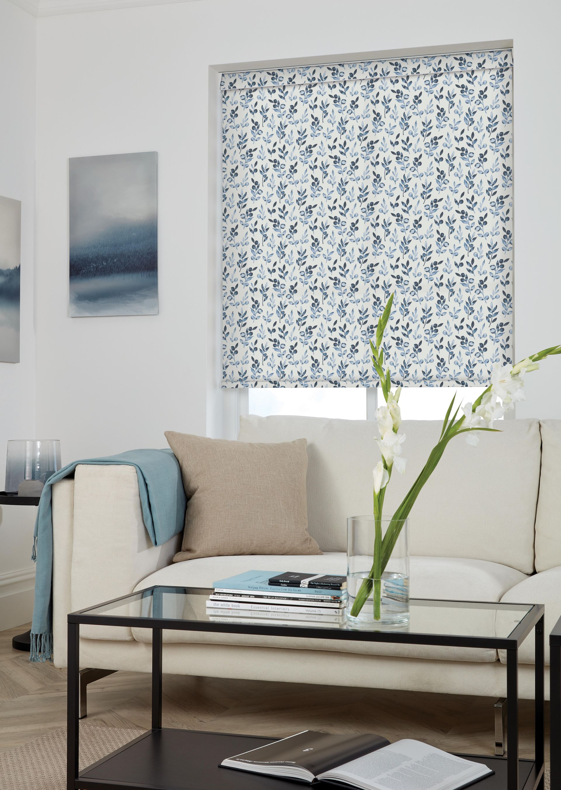 Living room with a white sofa, glass coffee table, and patterned window blinds.