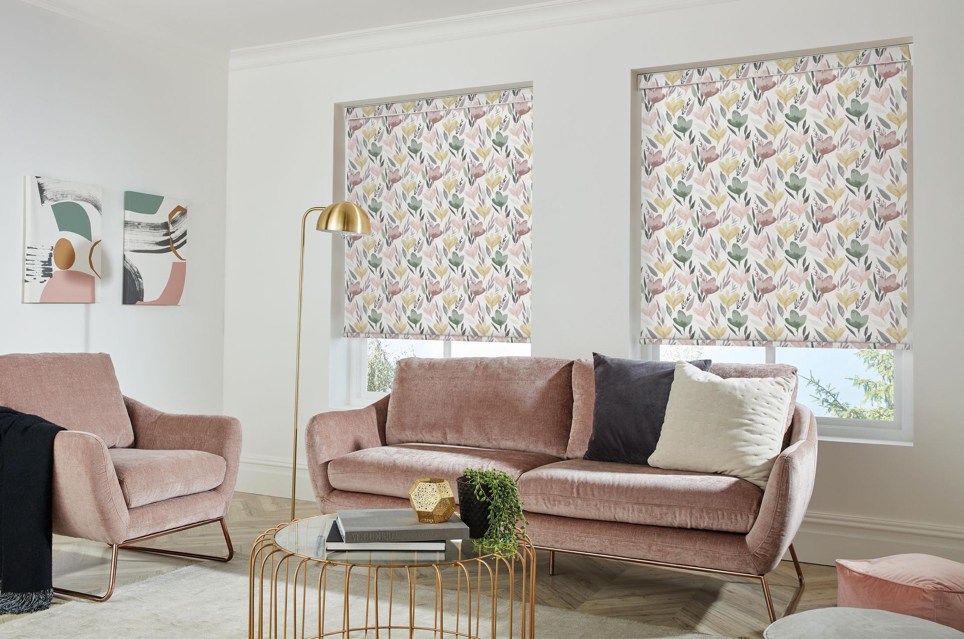 Living room with floral patterned roller blinds, pink velvet sofa and armchair, gold accents.