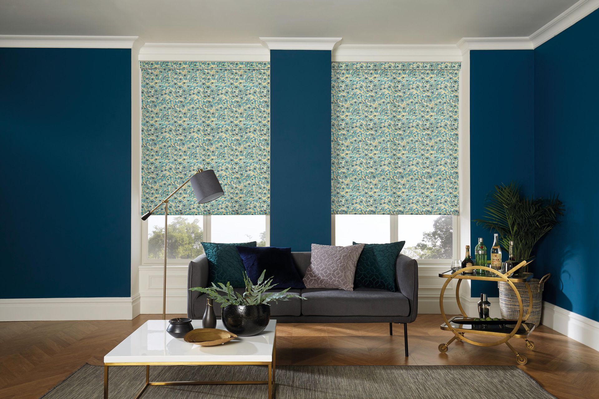 Blue-walled living room with floral blinds, sofa, and gold bar cart; hardwood floor and white trim.