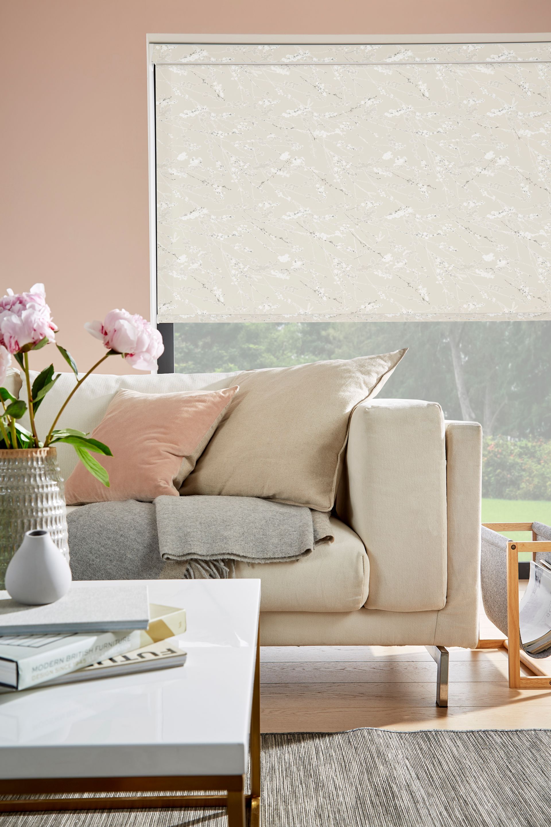 Living room with cream-colored couch, roller shade, pink wall, and flowers on a white coffee table.