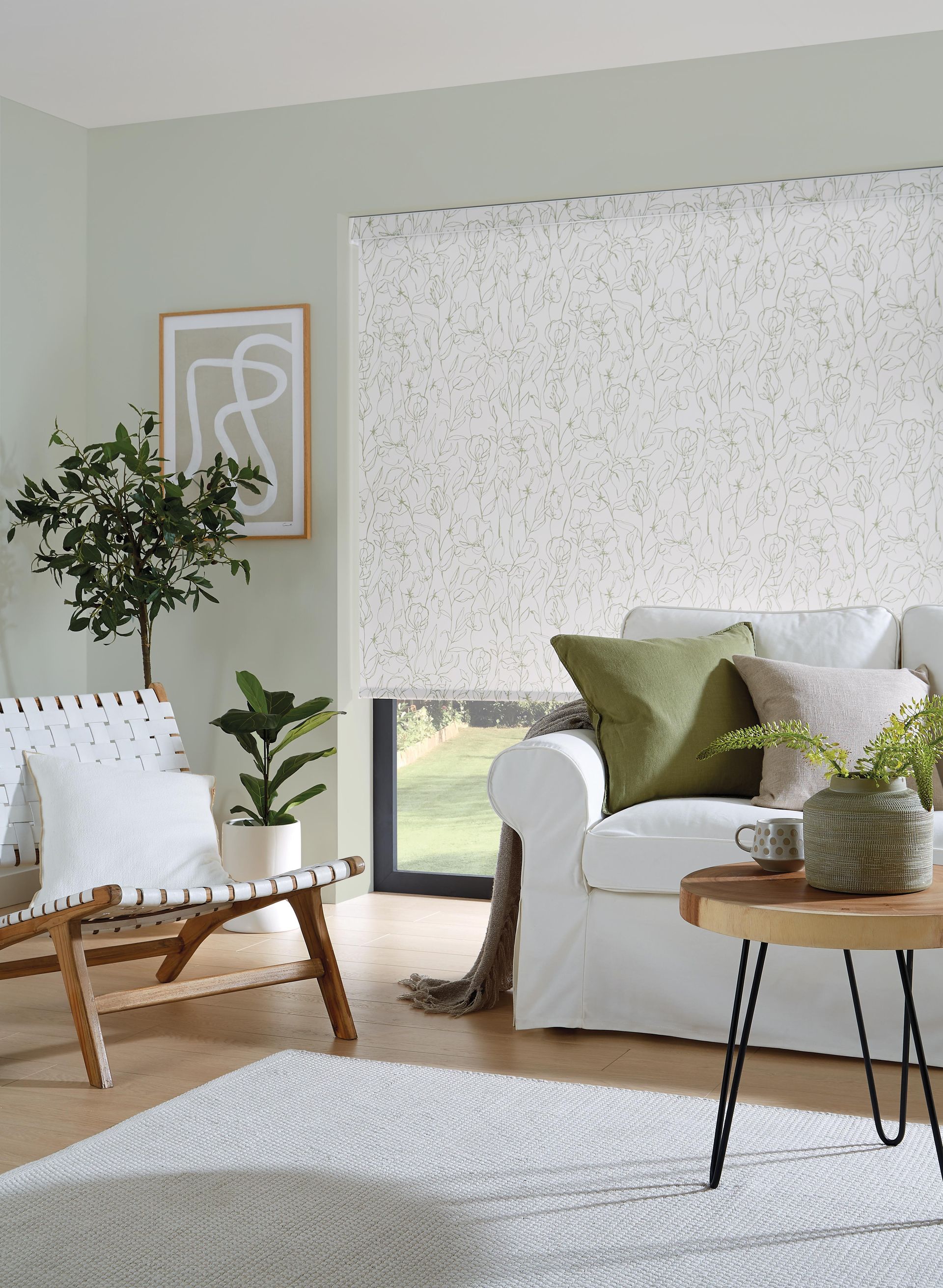 Living room with white sofa, textured rug, and light green walls, decorated with plants and art.